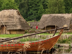 Foto da reconstrução de uma aldeia eslava com casas de madeira e palha e um barco