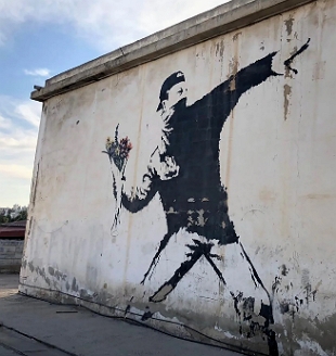 Pintura em parede de rua mostrando um homem vestido de preto atirando um buquê de flores