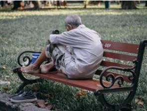Foto de um morador de rua sentado num banco de uma praça