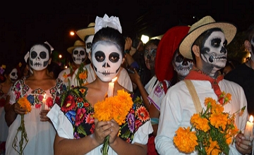 Foto de pessoas com o rosto pintado de caveira e segurando velas e flores