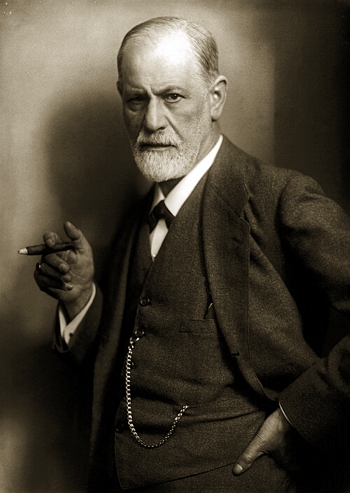 Sigmund Freud Foto de Freud, homem idoso de barba branca e calvo, segurando um charuto e vestindo terno e gravata.