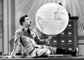 Chaplin com uniforme militar segurando um globo terrestre e sentado numa mesa.