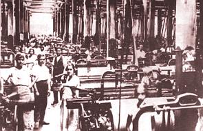 Foto da parte interna de uma indústria antiga do Brasil mostrando as máquinas e operários.