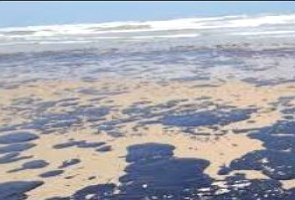 Foto mostrando manchas pretas de petróleo na areia de uma praia