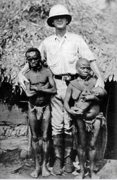 Foto de um europeu ao lado de dois pigmeus adultos e uma criança de colo