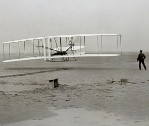 Foto em preto e branco mostrando um pequeno avião levantando voo e um homem ao lado