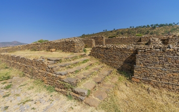 Ruínas do Palácio de Dungur Foto mostrando escadas e paredes pela metade, feitas de pedra.