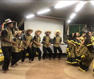 Homens e mulheres dançando com roupas típicas de cor amarelo e preto.