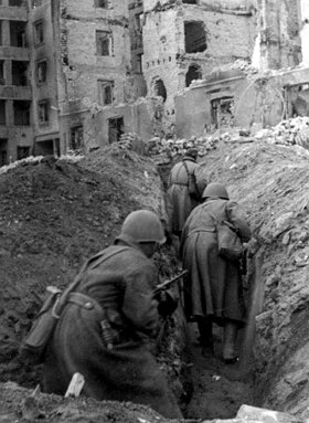 Foto de soldados num local com prédios destruídos pela guerra